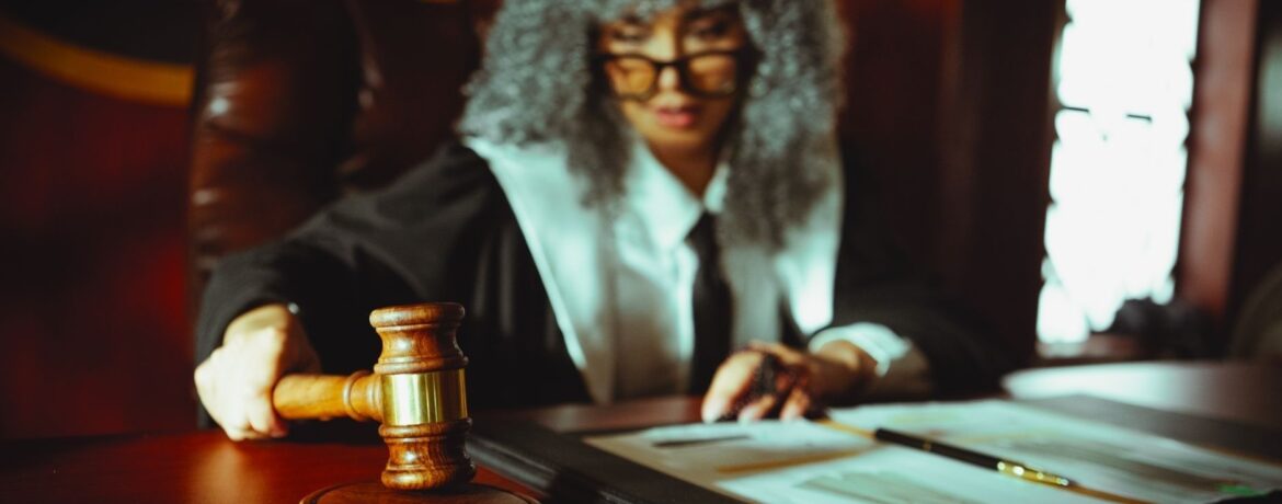 Judge holding a gavel beside legal documents on a courtroom bench