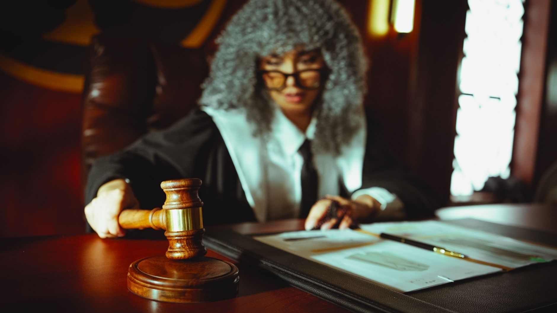 Judge holding a gavel beside legal documents on a courtroom bench